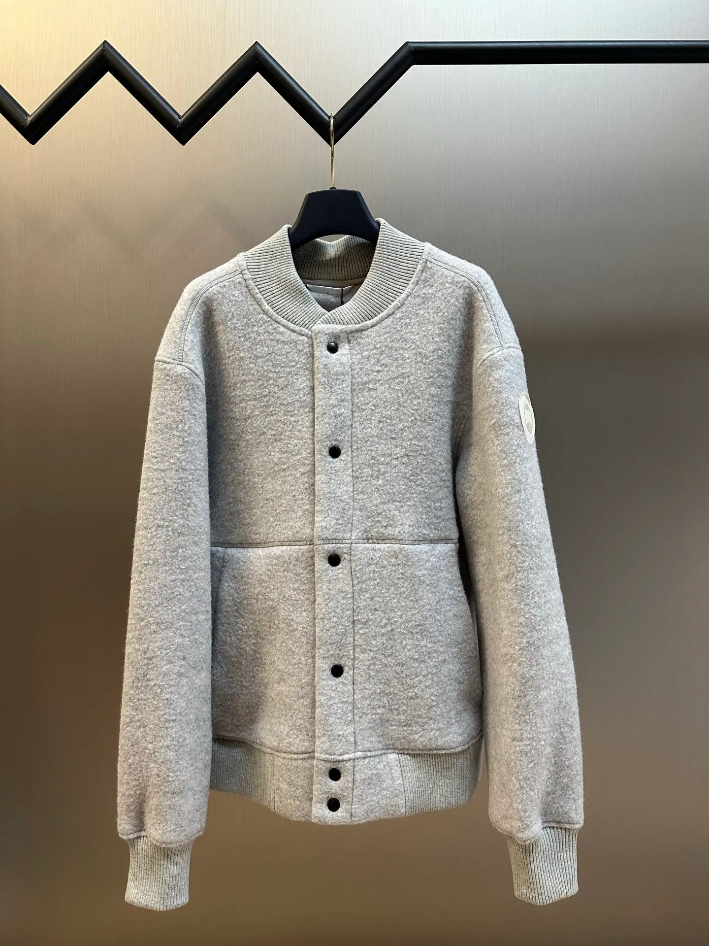P770 Canada Goose Fleece Badge Button Jacket The main fabric of this jacket is light gray wool blend fabric to improve the fabric's wear resistance, wrinkle resistance and warmth. Wool provides good warmth and a natural feel, while blended fibers enhance the fabric's practicality and durability.  The cutting process needs to ensure that the texture and color of the fabric are evenly distributed, especially with this light gray tone, to avoid chromatic aberrations. The stretchability of wool-blend fabrics needs to be taken into consideration when cutting pieces to ensure dimensional stability of the finished garment.  Use a sewing needle and thread suitable for wool-blend fabrics to avoid damage to the fabric during sewing. The sewing stitches are even and firm to prevent thread stripping.  The temperature needs to be controlled during ironing to avoid high temperature damage to the fabric while keeping the fabric smooth and crisp. The front and back body parts, sleeves and other main parts are stitched with flat seams to ensure a smooth silhouette. Align the fabric texture at the splices to keep the look neat.  The white circular armband on the left arm is an important part of the brand identity and is finely sewn to ensure it is strong and flat.  size：s m l xl